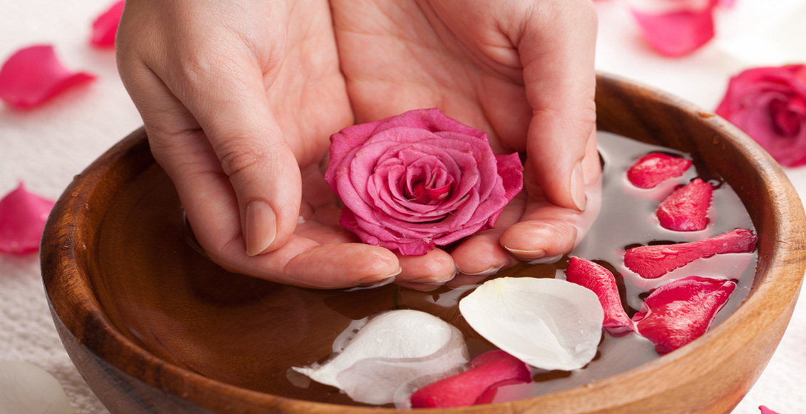 أهم نصائح استخدام سكراب السكر والليمون صورة يد تمسك وردة فوق وعاء فخاري به أوراق الورد وماءه