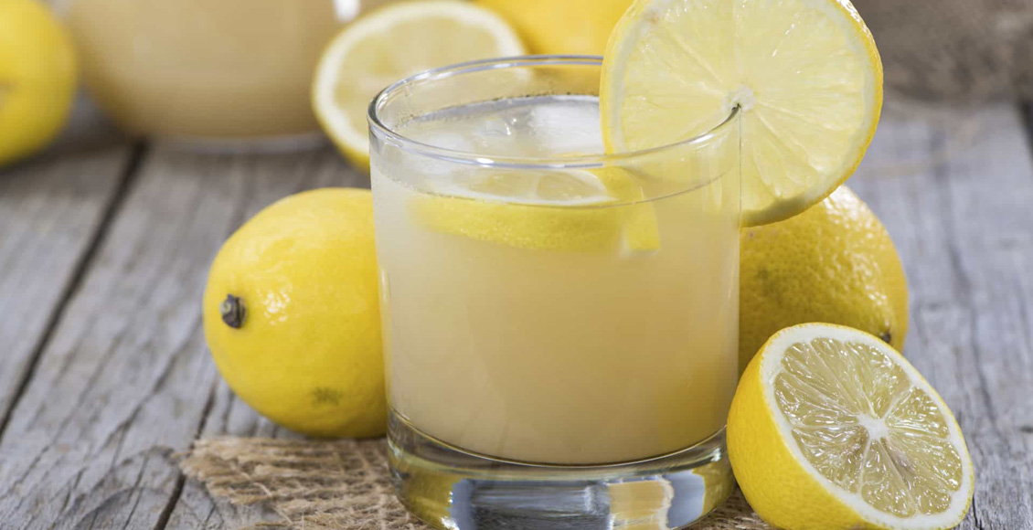 ما هي أضرار الليمون والسكر للوجه؟ كوب بع عصير ليمون وقطع منه إلى جواره الكثير من حبات الليمون وأنصاف الحبات